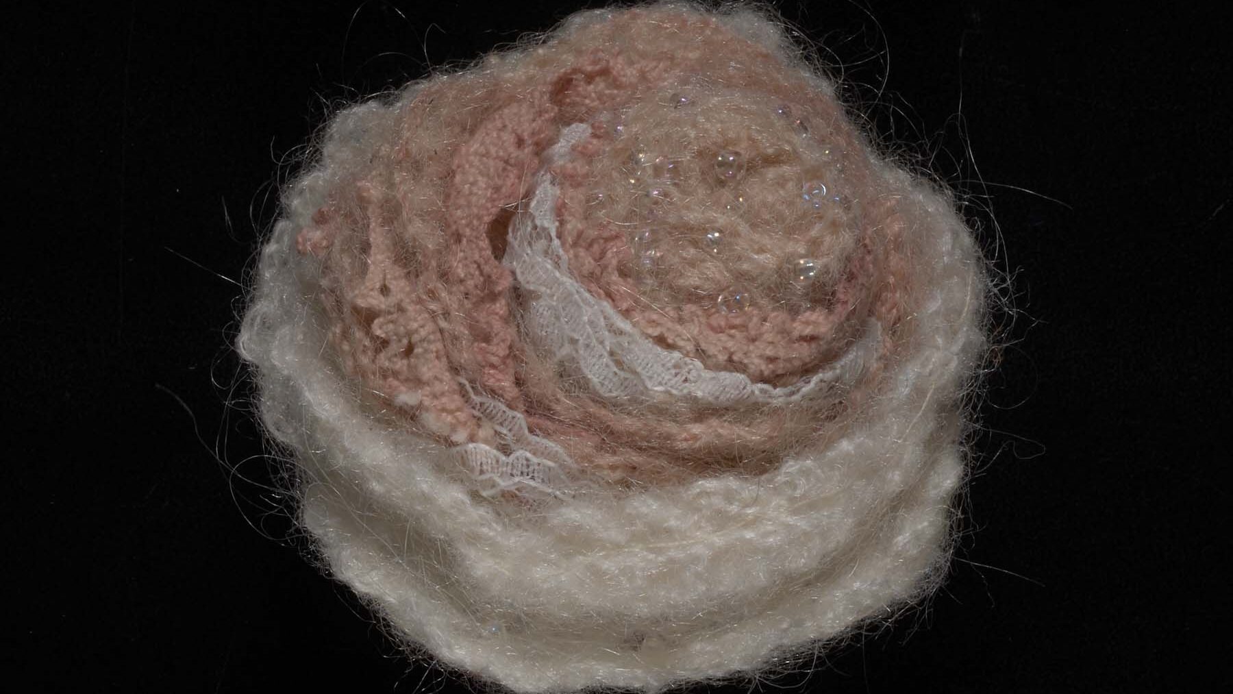 A close up of a flower, made from textiles. Light in colour (white and pinks).