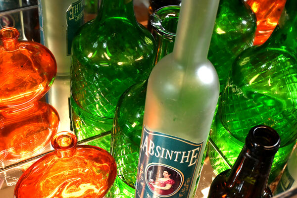 A photo of a handful of green and orange bottles, closely cropped. Mirror behind with reflection of bottles visable.