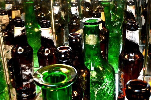 A photo of a handful of green and orange bottles, closely cropped. Mirror behind with reflection of bottles visable.