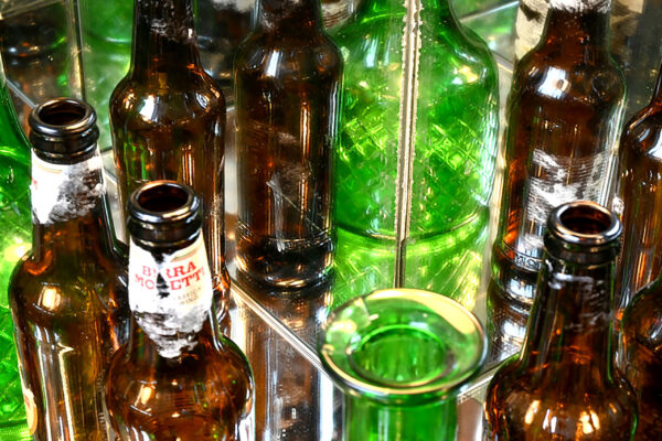 A photo of a handful of green and orange bottles, closely cropped. Mirror behind with reflection of bottles visable.