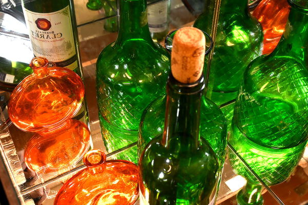 A photo of a handful of green and orange bottles, closely cropped. Mirror behind with reflection of bottles visable.
