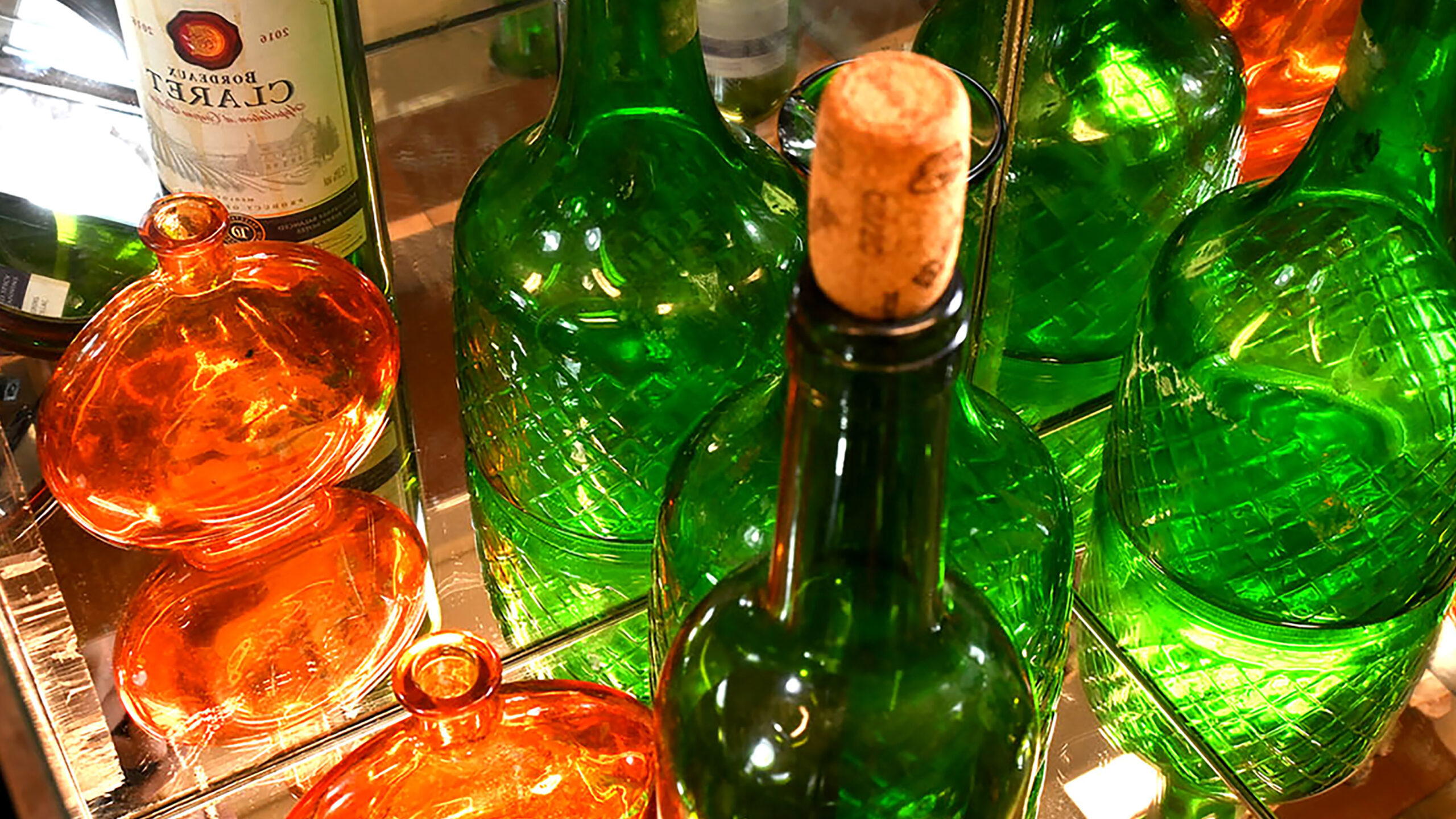 A photo of a handful of green and orange bottles, closely cropped. Mirror behind with reflection of bottles visable.