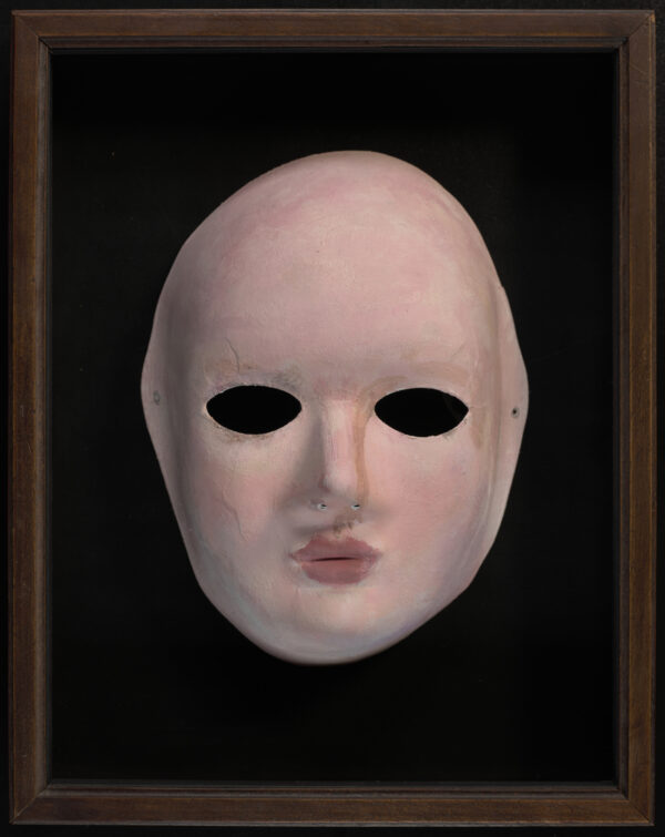 A paper mache mask. Pink in colour, photographed on a black background.