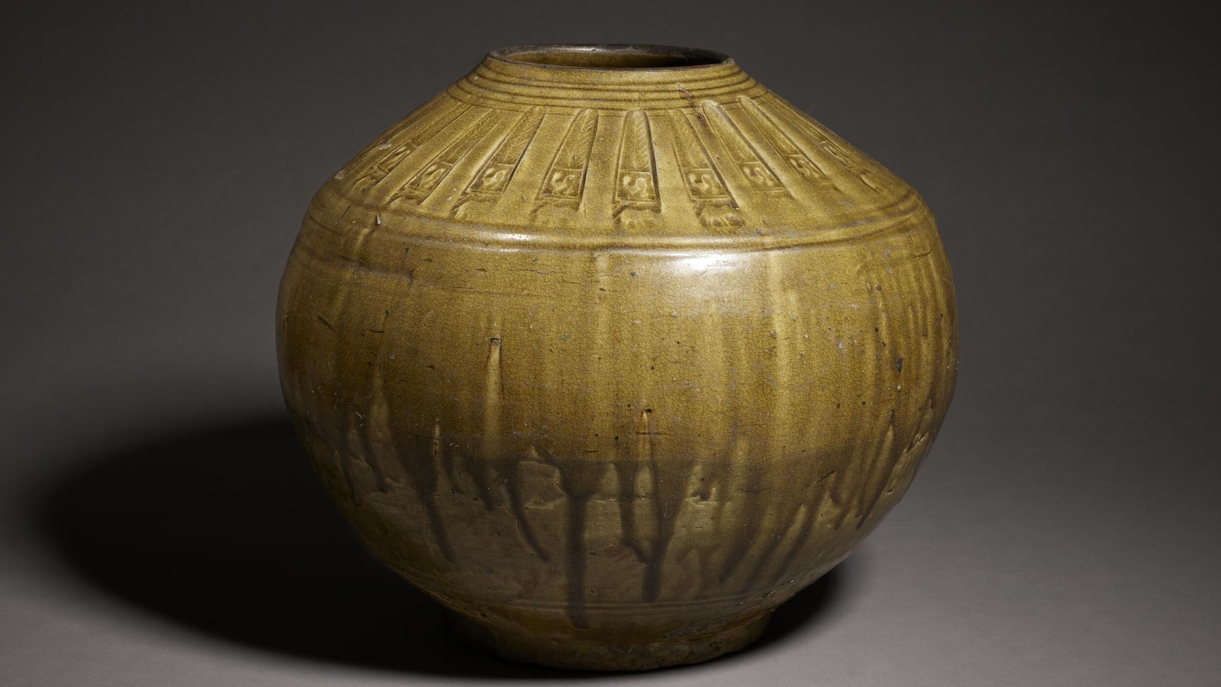 Photograph of a ceramic storage jar with an olive green dripping glaze.