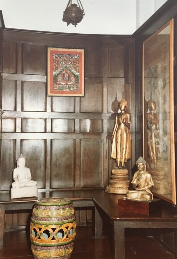 A room covered in wood, with a drum on the floor, two golden Buddha figures and a painting hanging from the wall