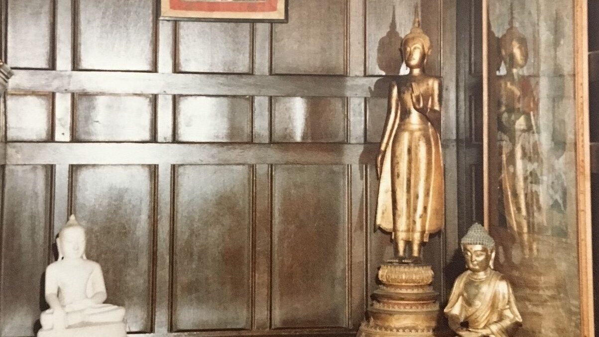 A room covered in wood, with a drum on the floor, two golden Buddha figures and a painting hanging from the wall