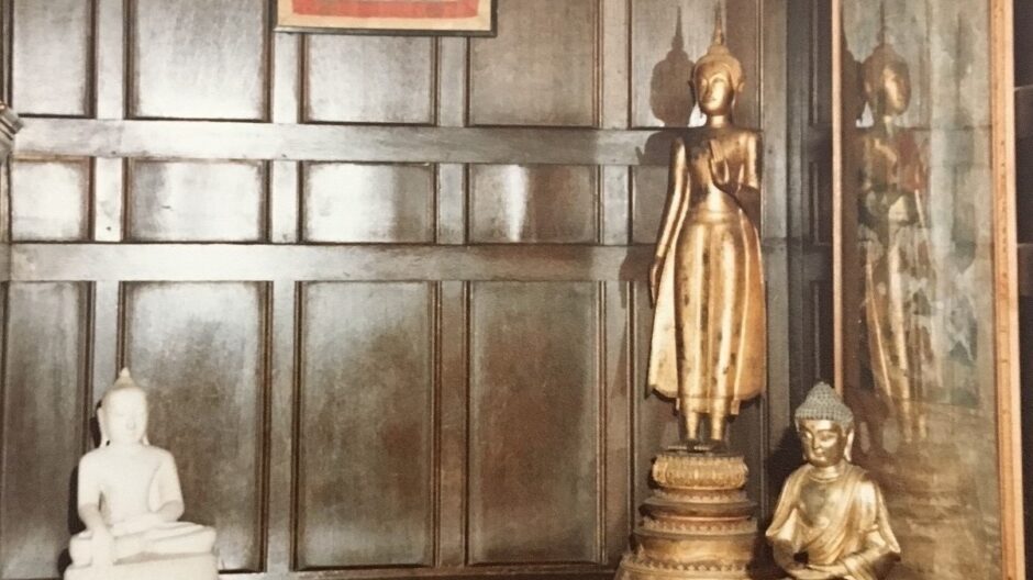 A room covered in wood, with a drum on the floor, two golden Buddha figures and a painting hanging from the wall
