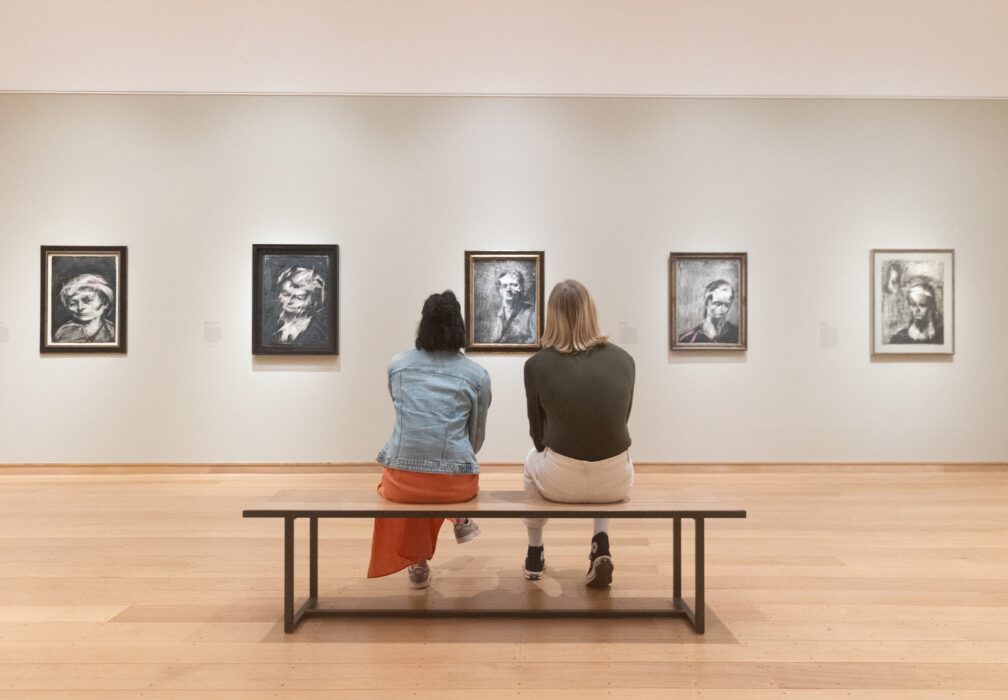 Two people sit on a bench admiring artworks in The Griffin Catalyst Exhibition: Frank Auerbach - The Charcoal Heads