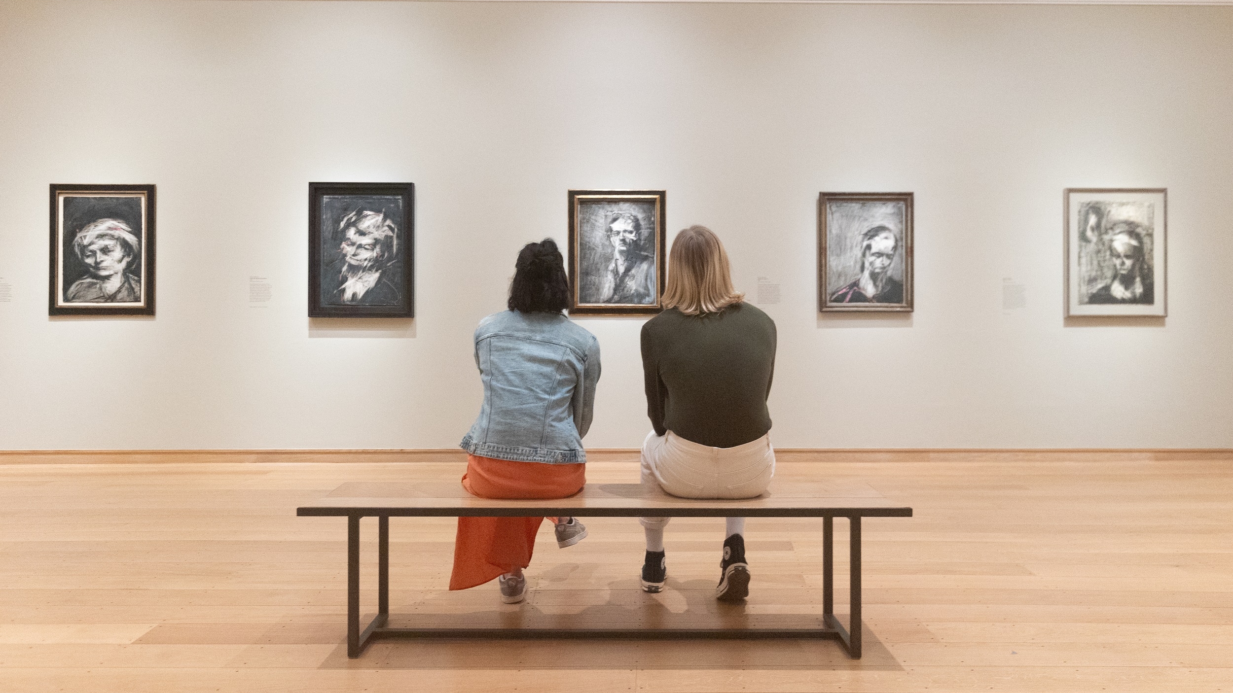 Two people sit on a bench admiring artworks in The Griffin Catalyst Exhibition: Frank Auerbach - The Charcoal Heads