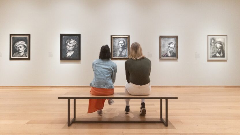 Two people sit on a bench admiring artworks in The Griffin Catalyst Exhibition: Frank Auerbach - The Charcoal Heads