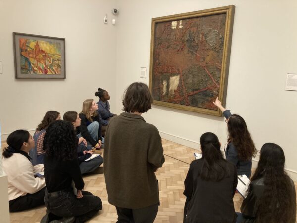 a group of young students sitting in one of the Courtauld's galleries and pointing at a paiting
