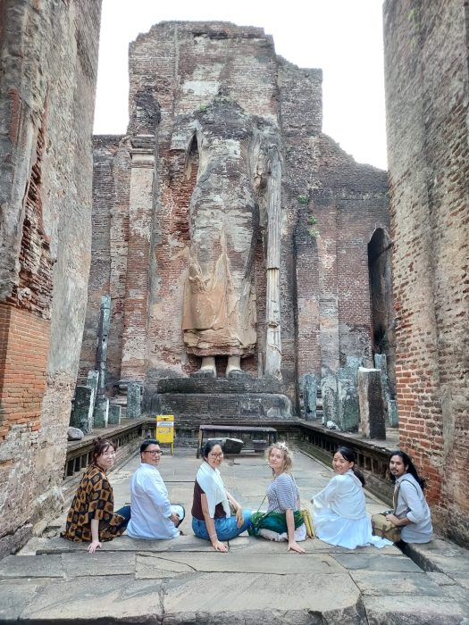 six students sit in a row on the steps of a Sri Lankan temple ruin