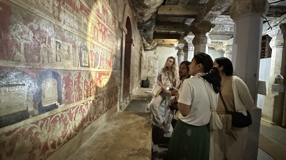 A group inspecting a wall painting using a torch for raking light