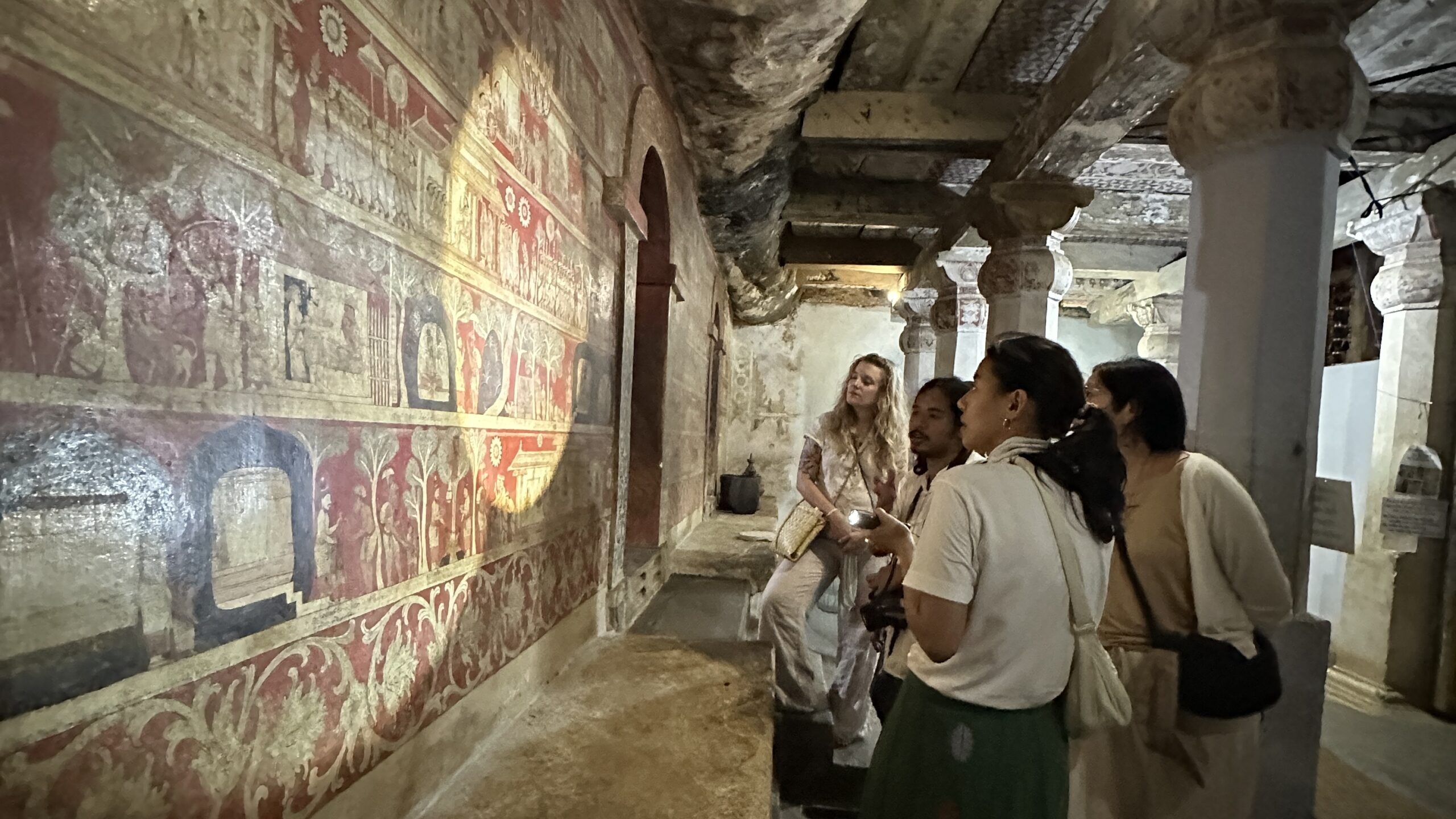 A group inspecting a wall painting using a torch for raking light