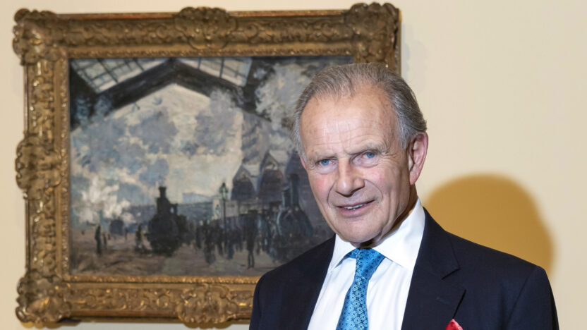 Christopher Mclaren with a suit and blue tie standing in front of an impressionist painting with a gilt frame