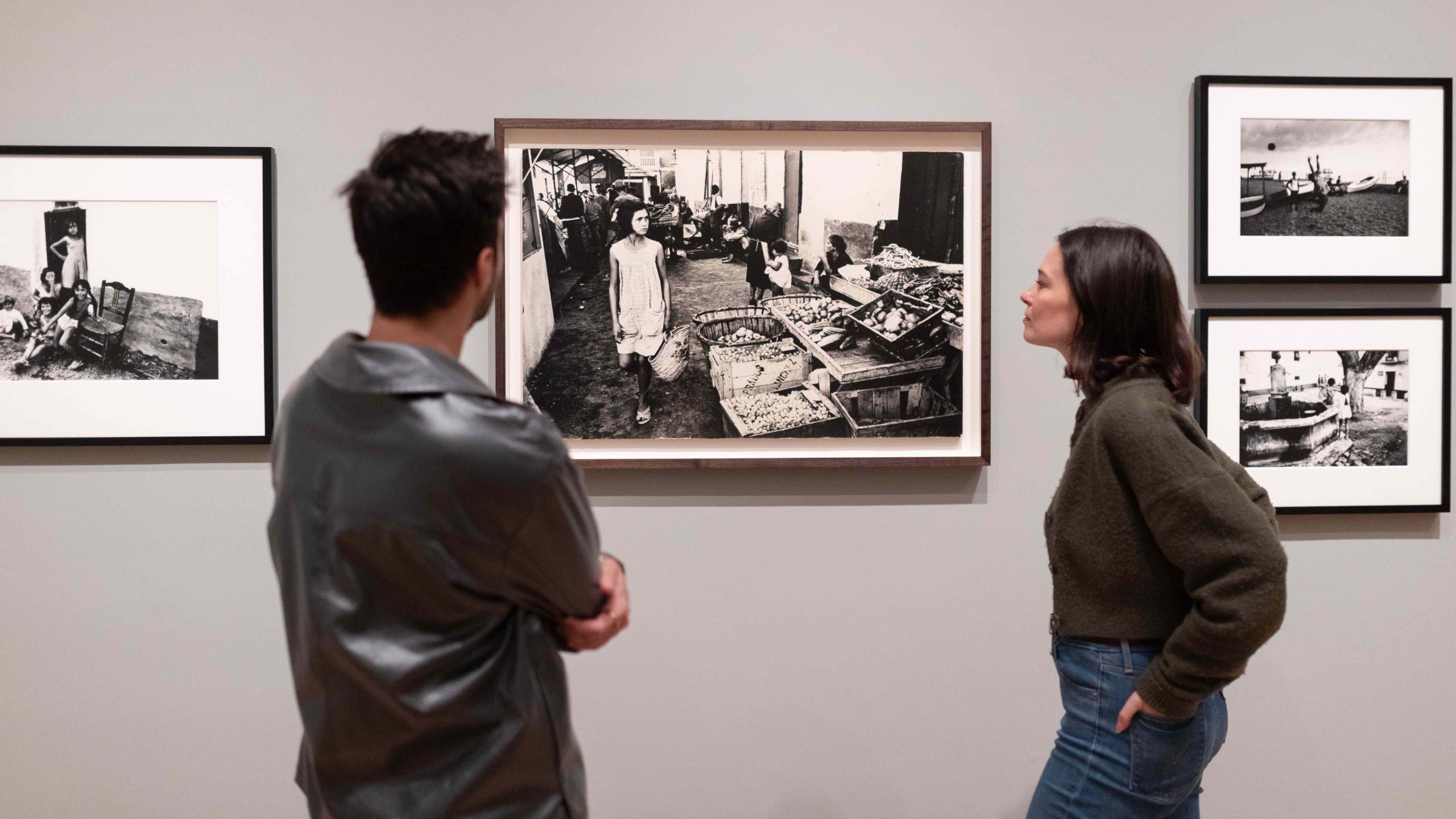 Two people looking at a photograph of a girl in a market in Spain, in the Roger Mayne: Youth exhibition at The Courtauld Gallery.
