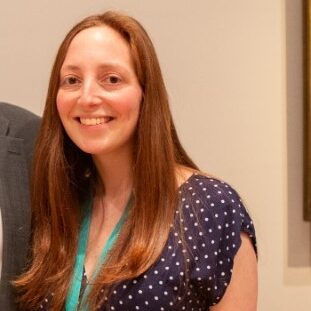 a woman and a man holding each other and smiling, behind them two paintings by Van Gogh hanging on a wall