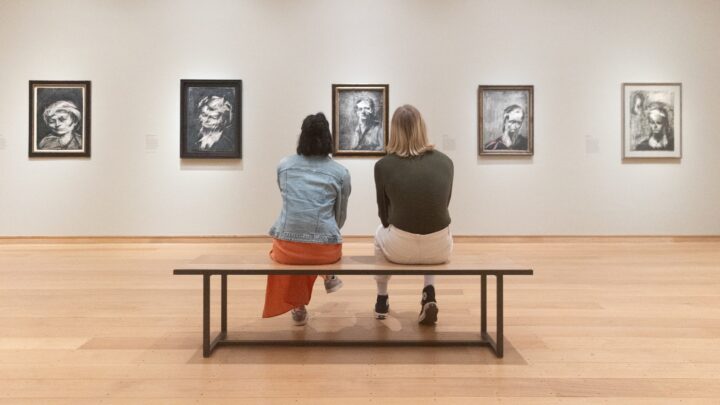 Two people sit on a bench admiring artworks in The Griffin Catalyst Exhibition: Frank Auerbach - The Charcoal Heads