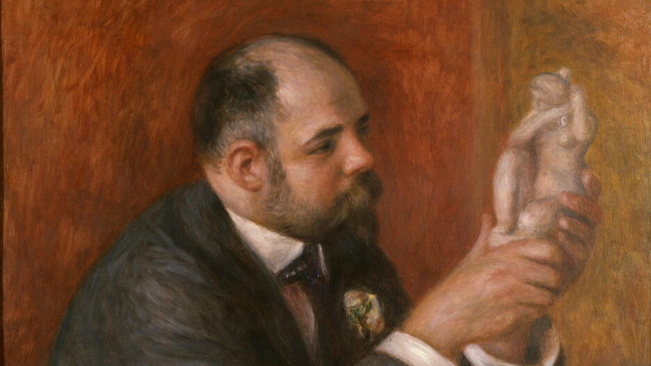 A man sits at a table and inspects a statue