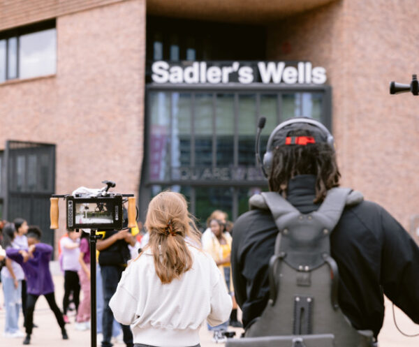 Two people stand in the foreground of the photograph in front of a building with signage that reads 