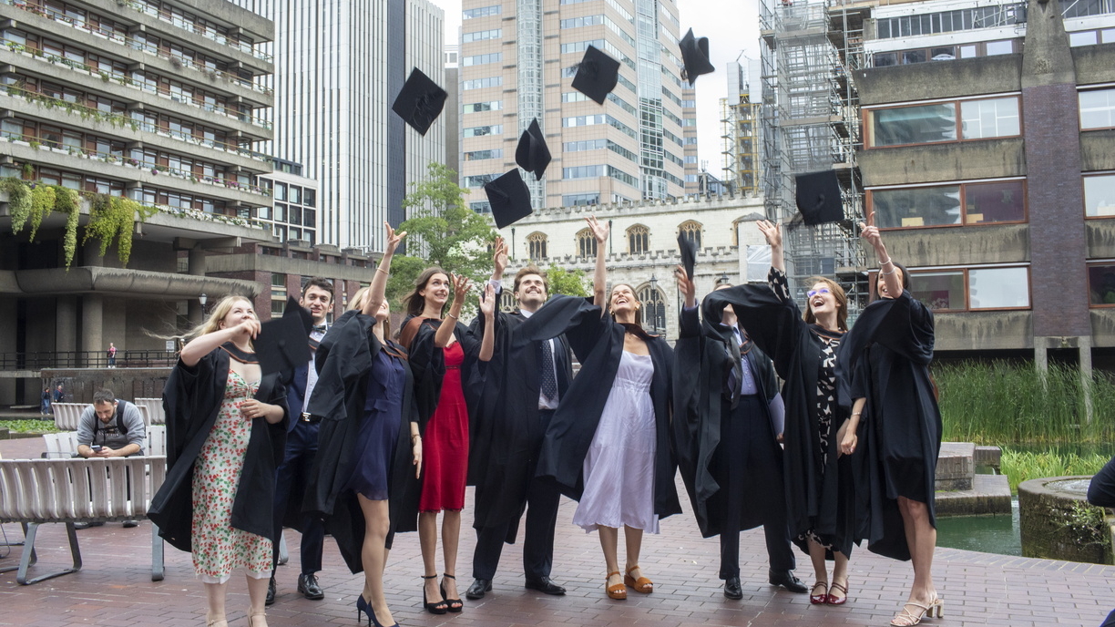 A group of students at The Courtauld Graduation 2024 throwing their caps in the air, at the Barbican courtyard.