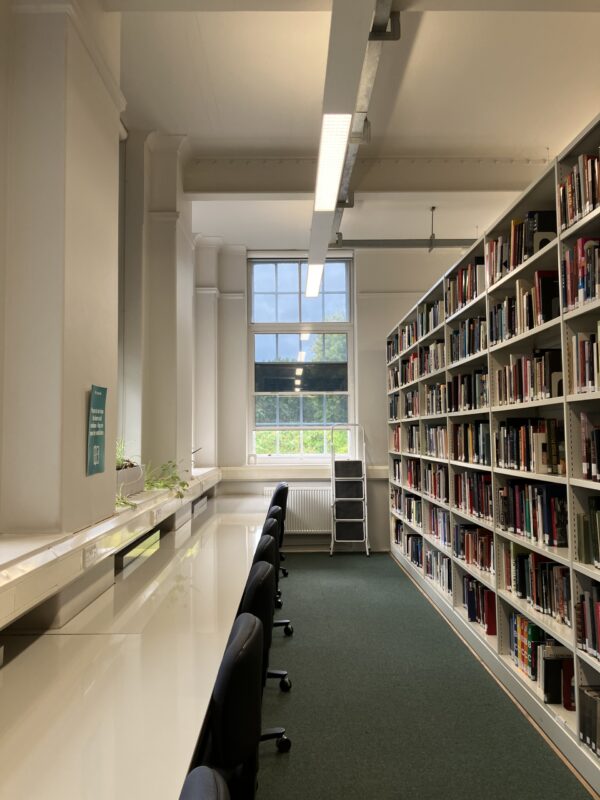 The Courtauld library space, with a row of desks backing onto a long shelving unit of books.