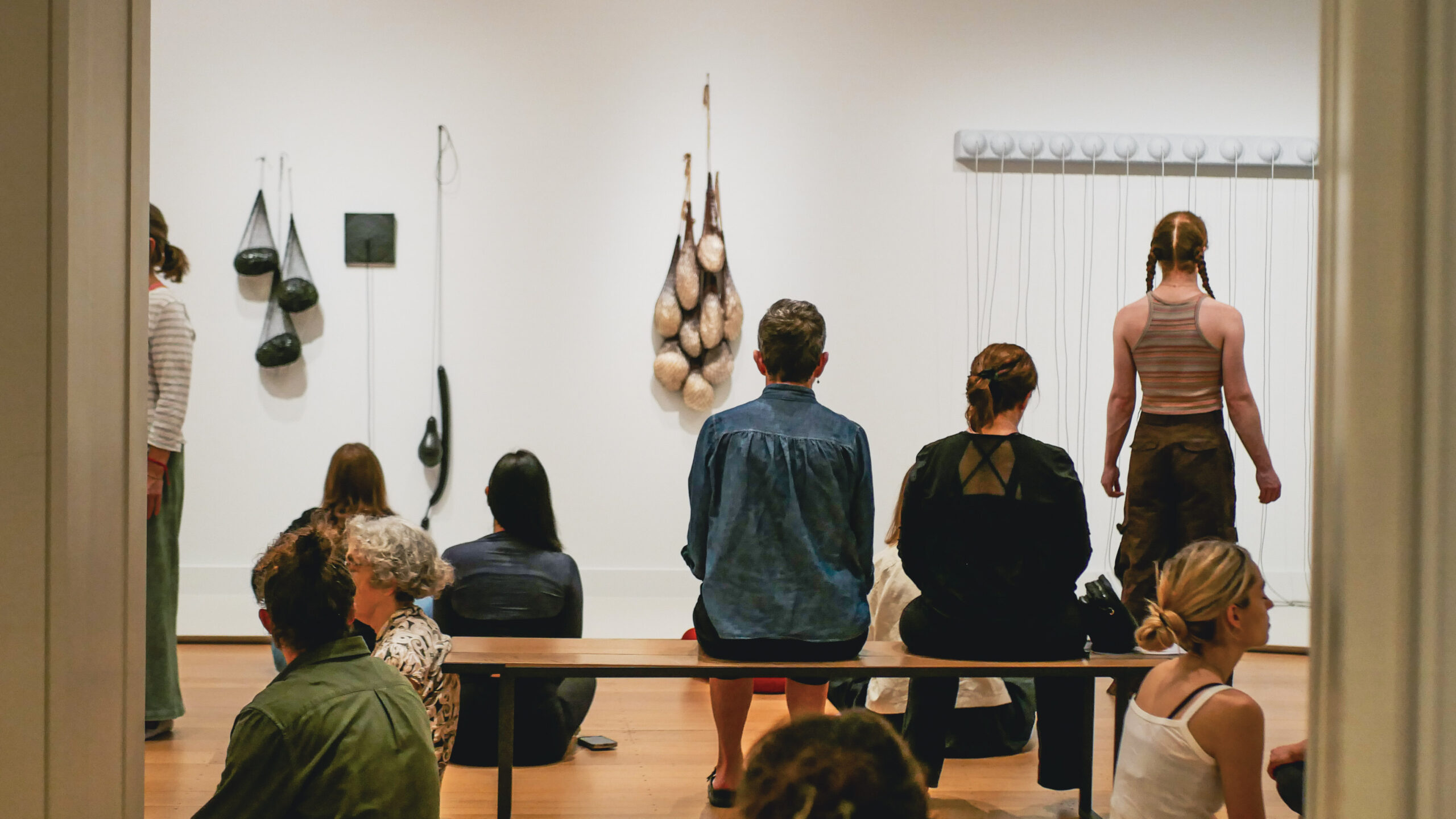 a group admire the artworks in an exhibition, some are seated on a bench and others on the floor. Abstract erotic is the exhibition.