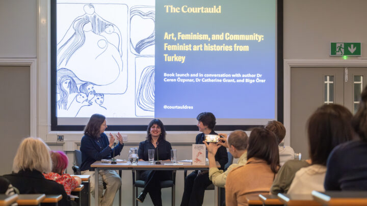 a panel of three women discuss in front of a busy lecture theatre