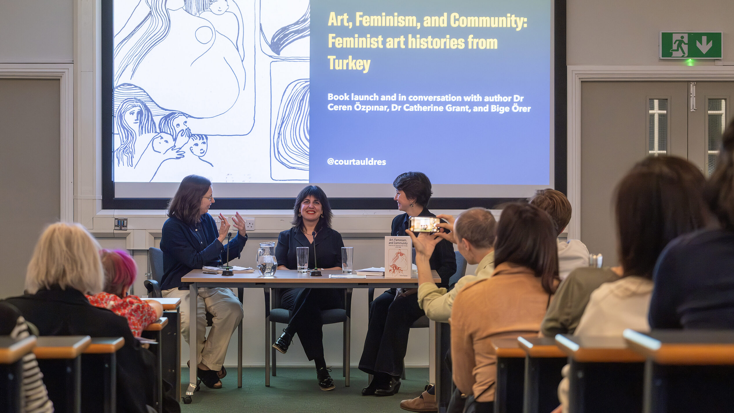 a panel of three women discuss in front of a busy lecture theatre
