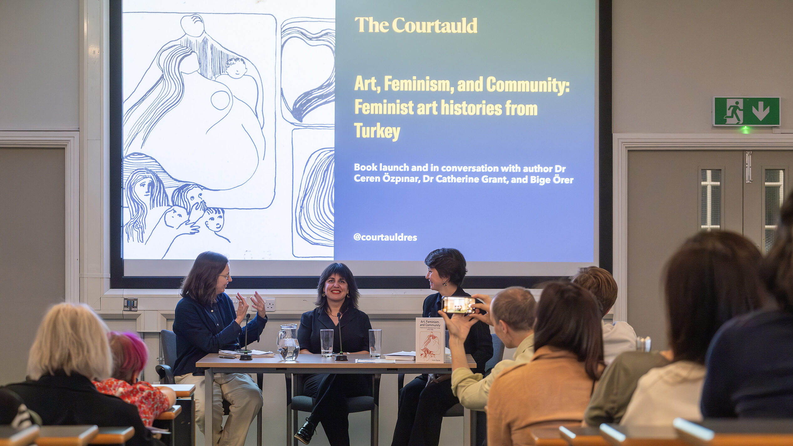 a panel of three women discuss in front of a busy lecture theatre