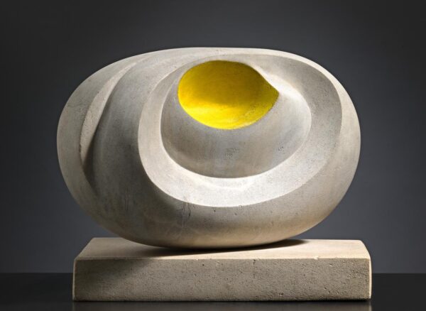 A marble sculpture with sweeping spherical curves, and a yellow dot in the centre. It sits on a marble plinth and dramatic lighting casts a strong shadow against a dark background.