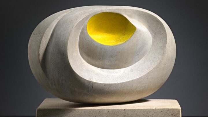 A marble sculpture with sweeping spherical curves, and a yellow dot in the centre. It sits on a marble plinth and dramatic lighting casts a strong shadow against a dark background.