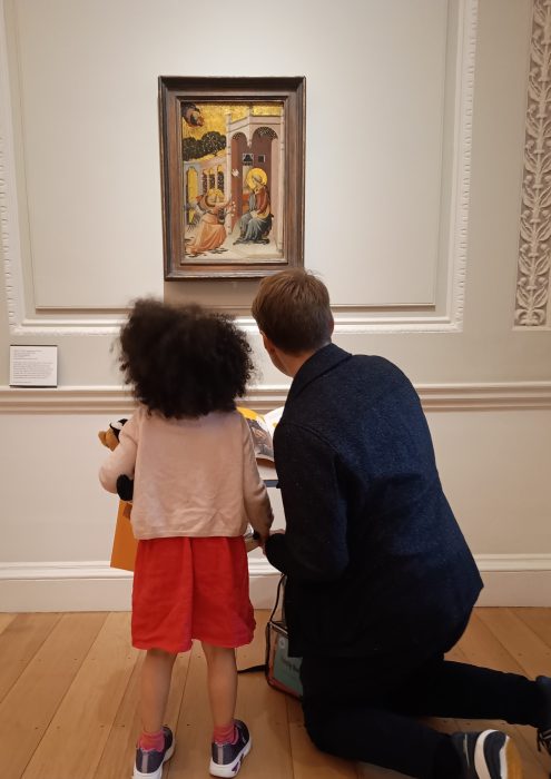 a child and a grown up looking at a painting on a wall