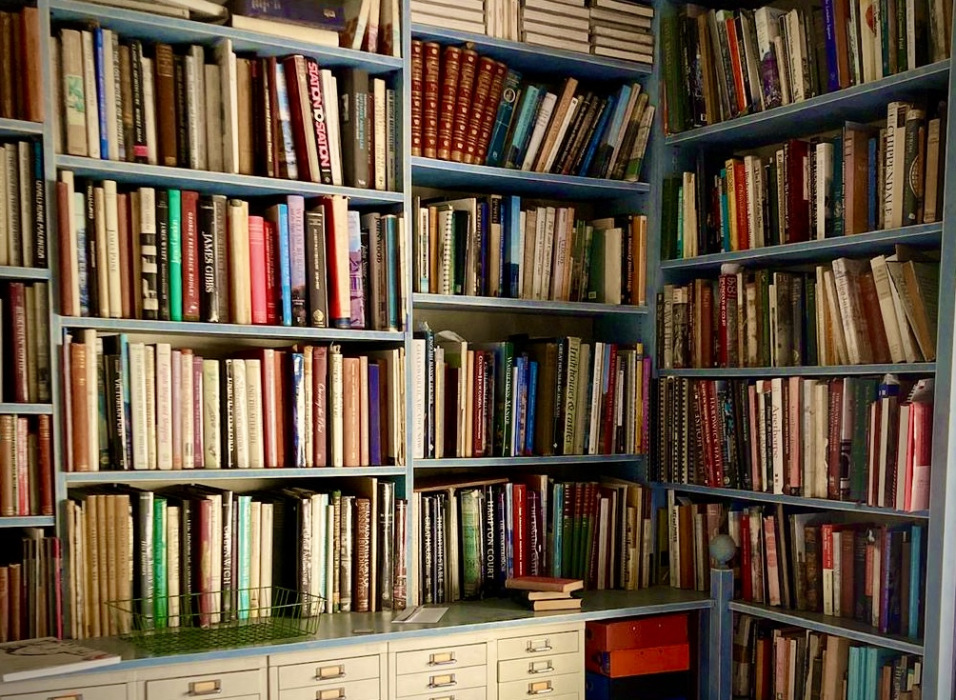Photograph or a coner-side floor to ceiling bookshelf, painted green, filled with books on architectural history.