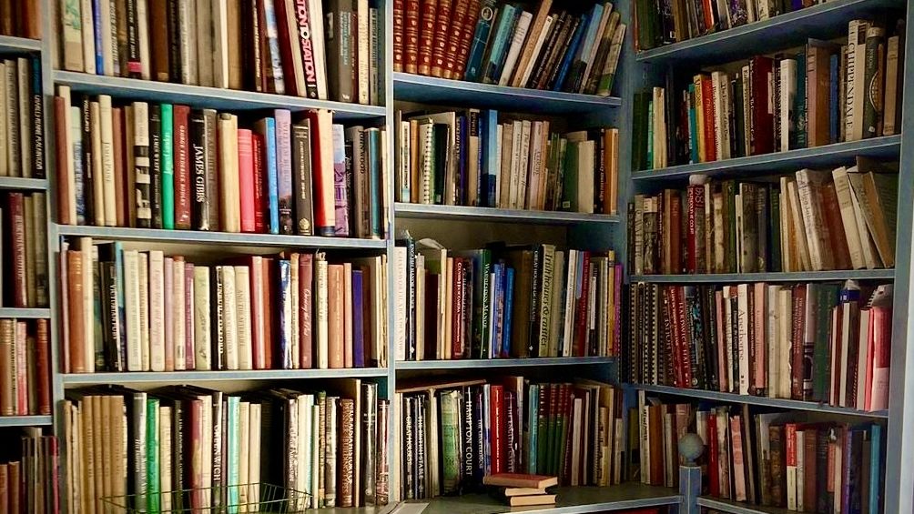 Photograph or a coner-side floor to ceiling bookshelf, painted green, filled with books on architectural history.