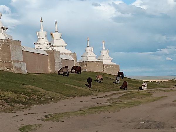 A white temple like building sits in a grassy landscape with grazing horses.