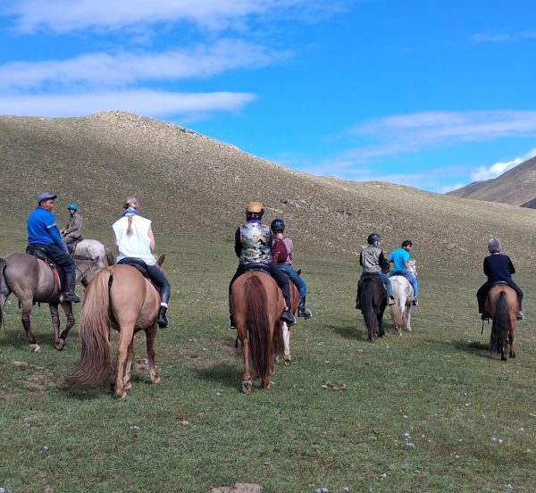 a small group of people on horseback ride trek across the Mongolian landscape.