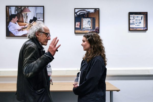 Two people in earnest, smiling conversation in front of two artworks in a classroom setting.