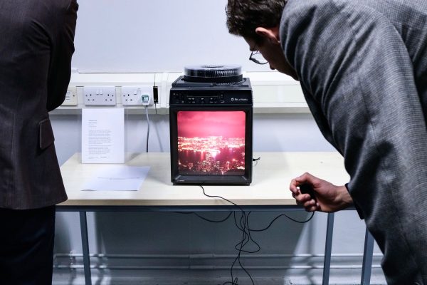A man leans in to watch a video artwork on an old VHS monitor, set on a classroom table.