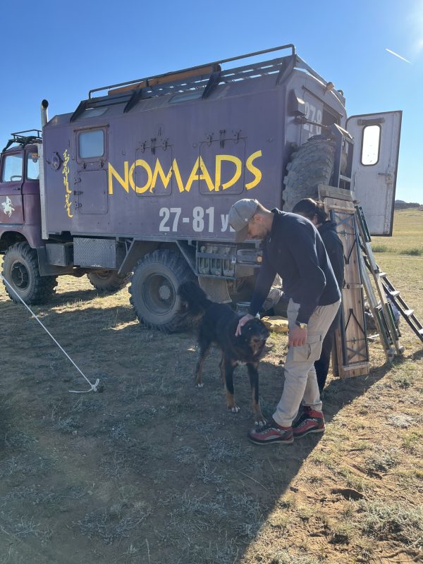 a large truck with NOMADS written on the side. A man with a dog stands in front of it.
