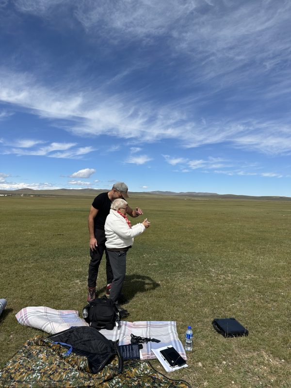 two figures converse whilst looking at a camera in a Mongolian landscape.