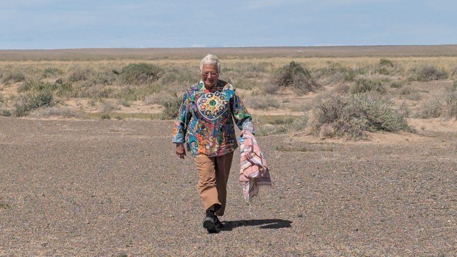 Professor sussan Babbaie walks towards the camera in adesert landcaspe wearing a colourful tunic.