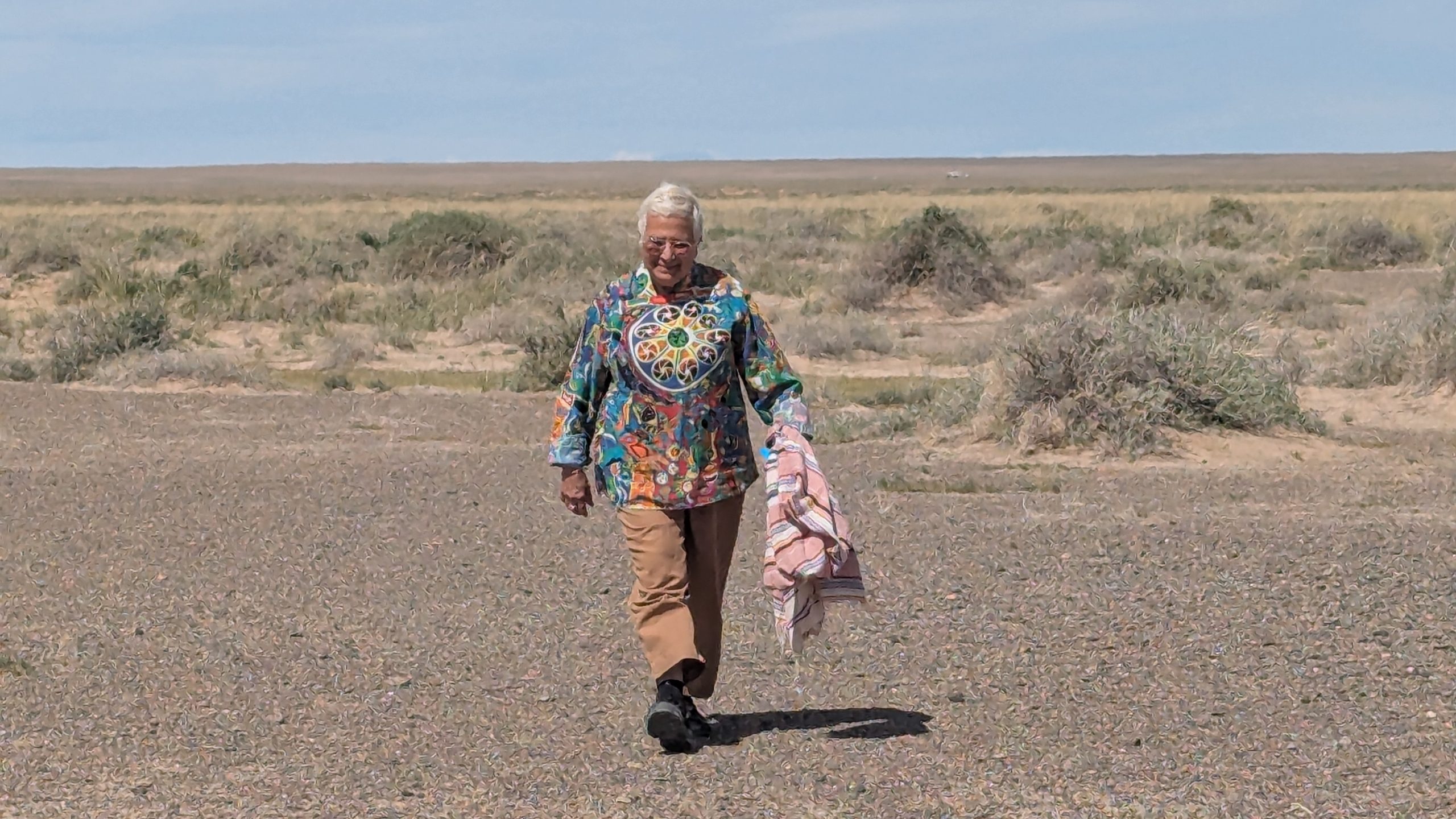 Professor sussan Babbaie walks towards the camera in adesert landcaspe wearing a colourful tunic.
