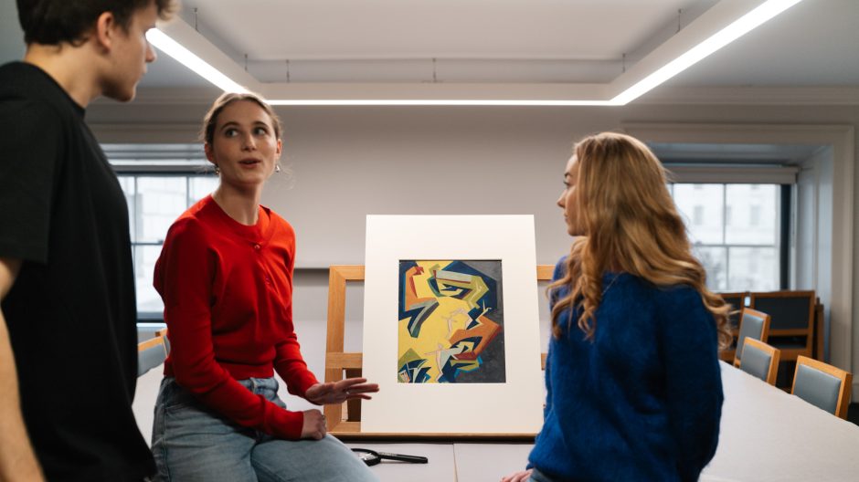 two female student and a male student talking to each other looking a a print
