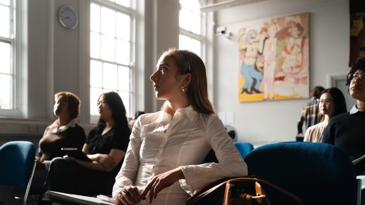 a close up of a female student with long hair sitting on a chair in a seminar room, looking away