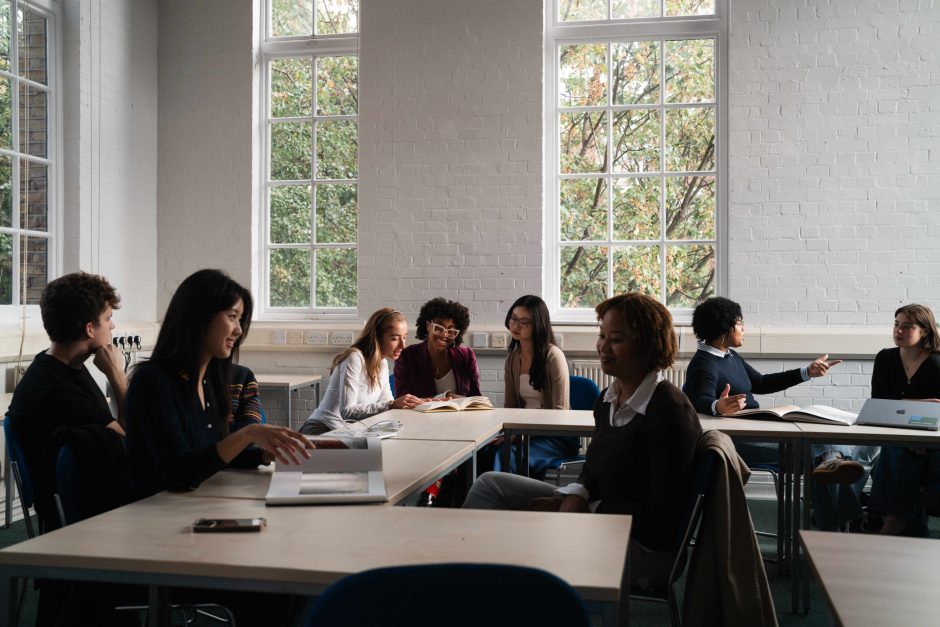 A group of students sitting in a seminar room, around an L-shaped arrangement of tables.