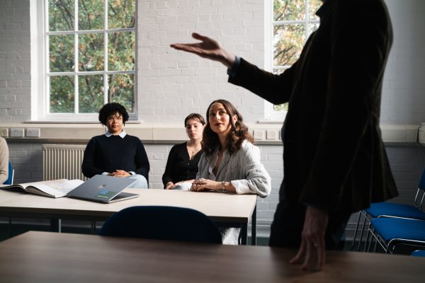 three female students sitting in a seminar room looking up at a tutor who's standing and pointing at something out of sight