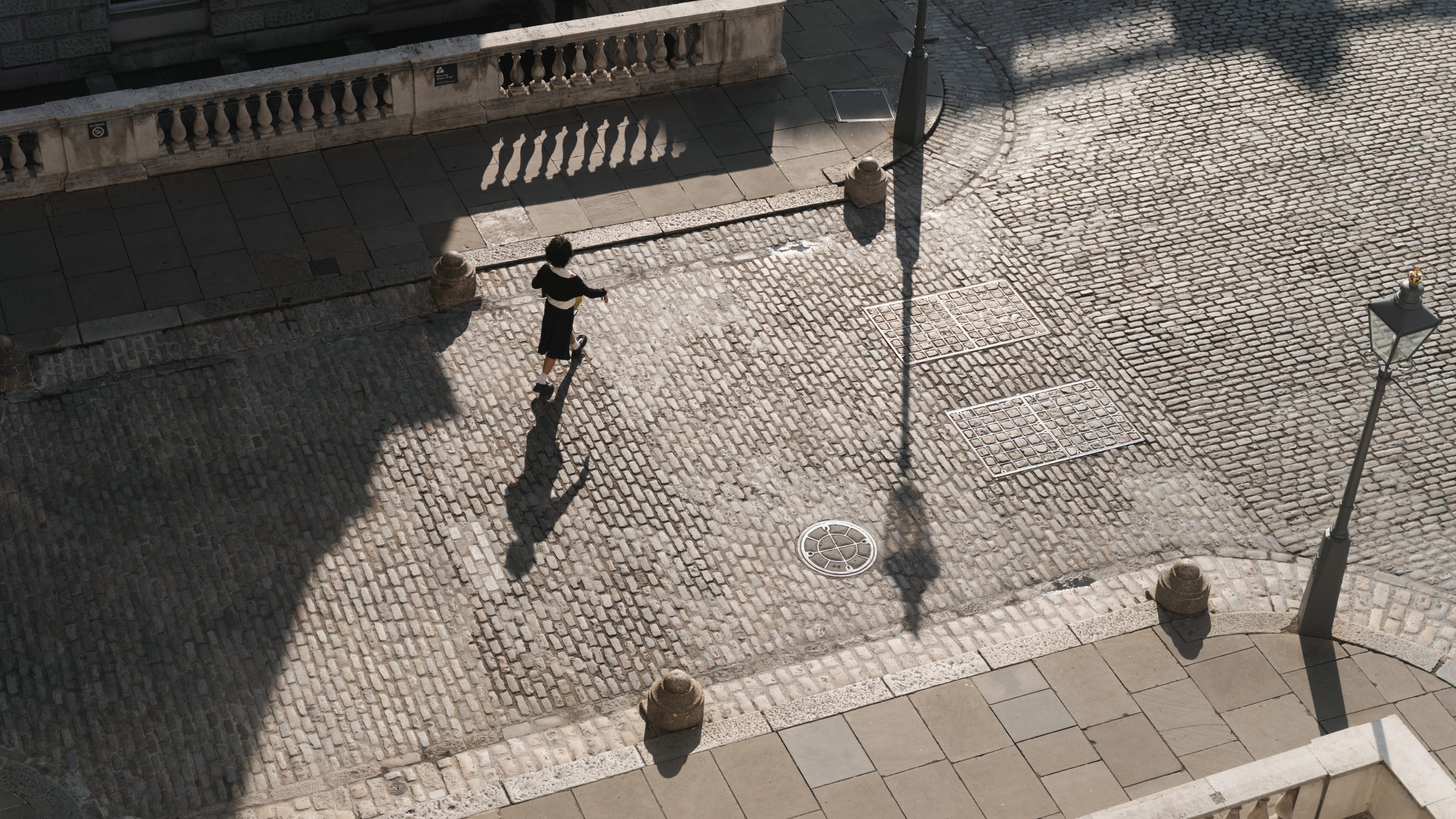 A photograph of someone walking into Somerset House, taken from above, sun on the white cobbles.