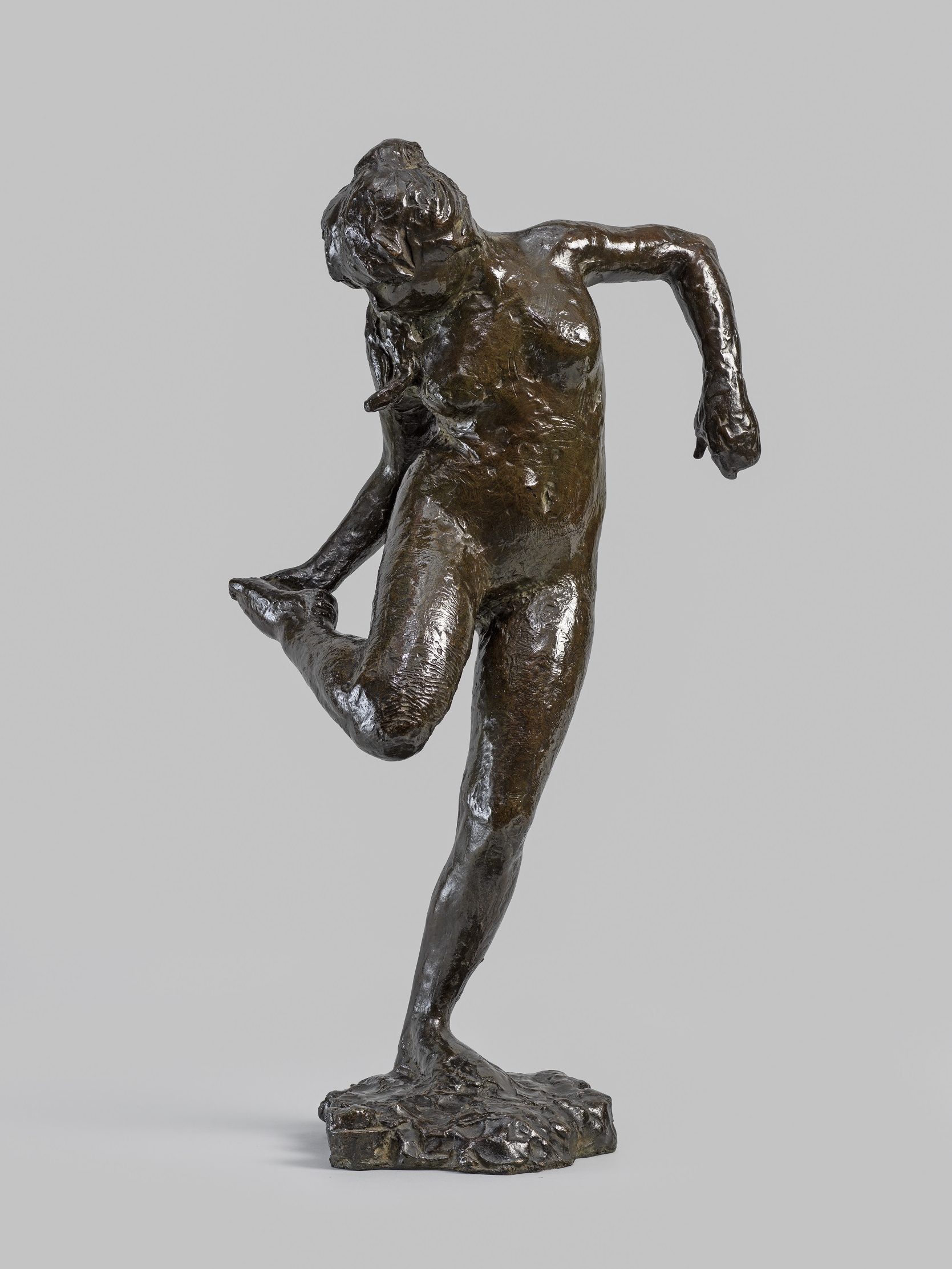 A bronze sculpture of a dancer looking at the sole of her right foot