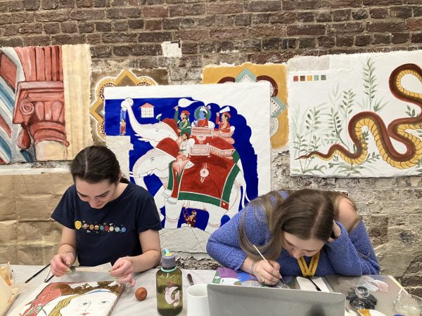 Two students painting, with various colourful artwork in the background.